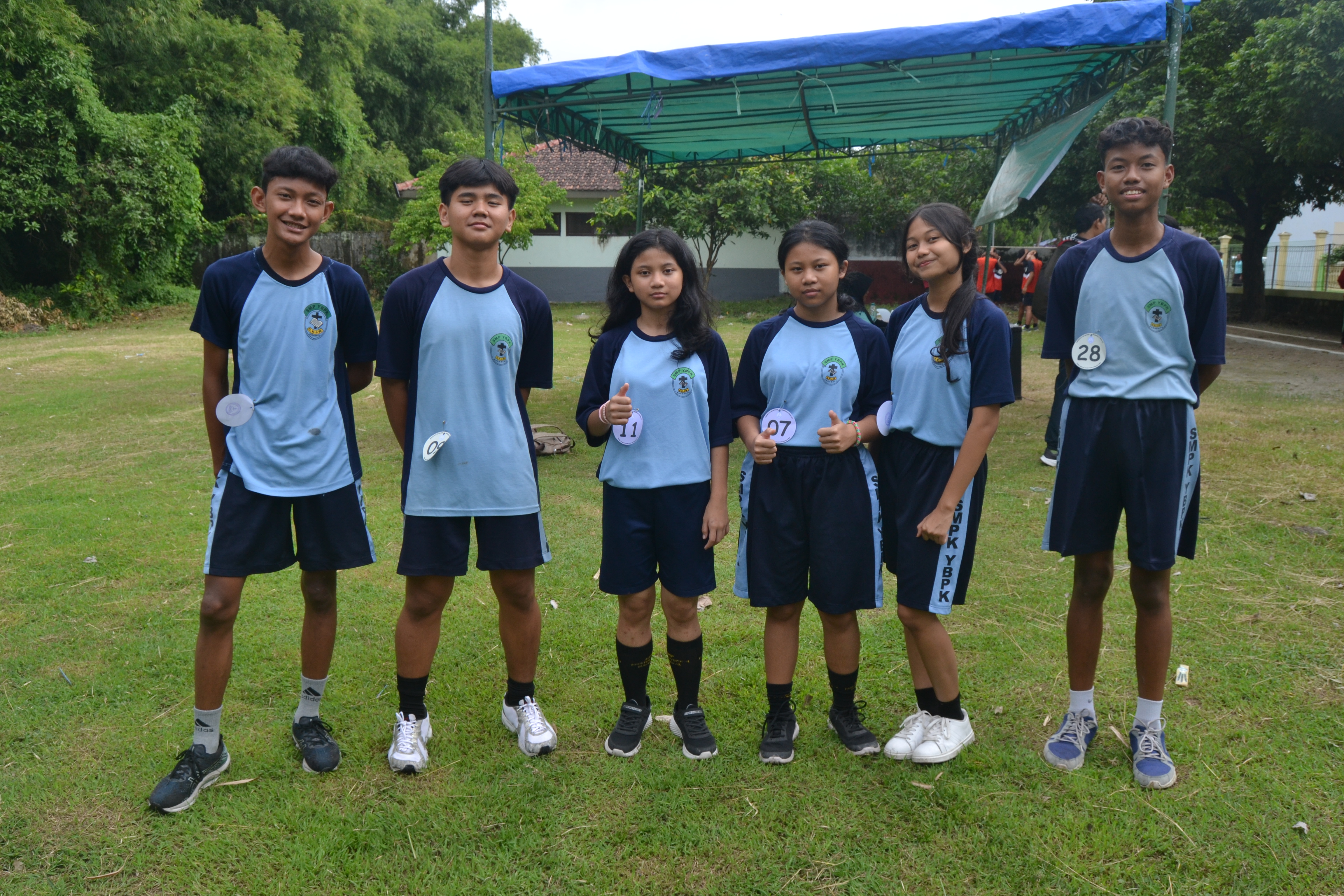 Murid berpose sambil tersenyum di lapangan rumput